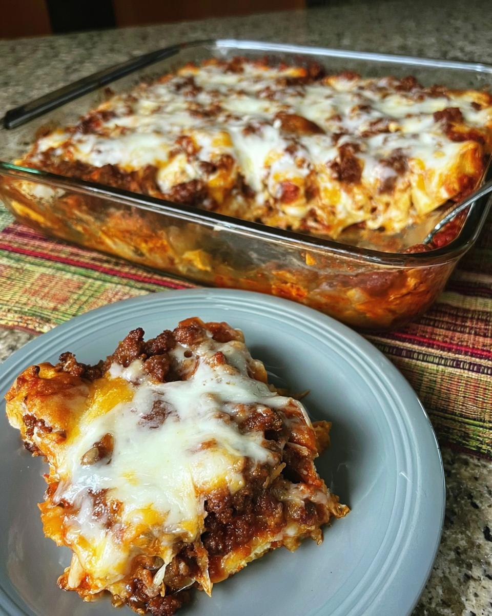 A close-up of a serving of Sausage Pizza Casserole on a blue plate, with the main baking dish visible behind it.