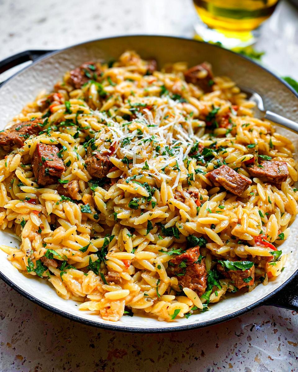 Nahaufnahme des Bestes Orzo-Abendessen mit Fleischstücken, Petersilie und geriebenem Käse in einer gusseisernen Pfanne.