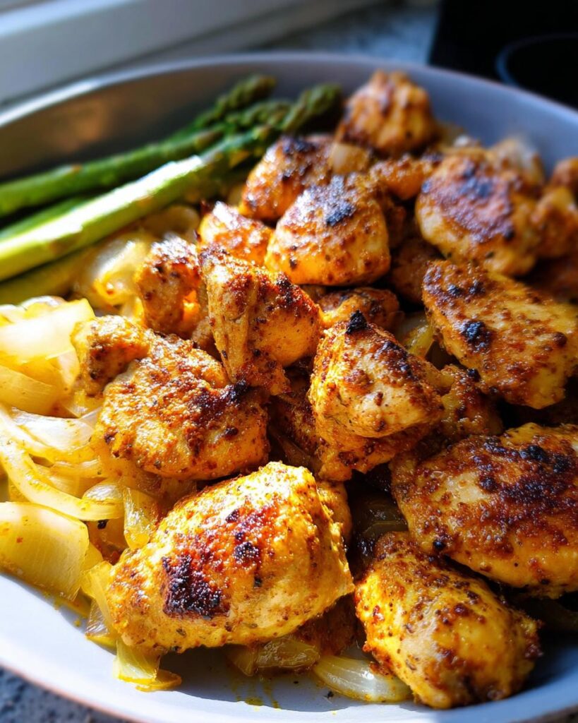 Nahaufnahme von gebratenen, gewürzten Hähnchenstücken mit sautierten Zwiebeln und Spargel – Teil des Einfaches Hähnchen Rezept.