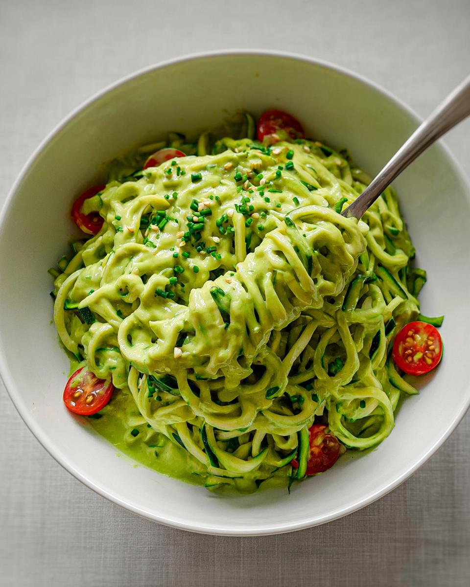 Nahaufnahme von Vegane Zucchini-Nudeln mit cremiger, grüner Avocado-Limetten-Sauce und Kirschtomaten.