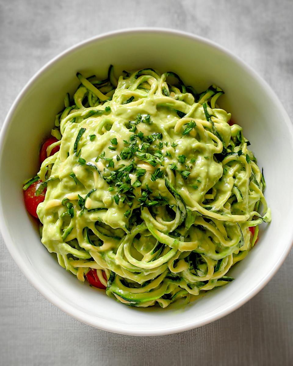 Nahaufnahme von Vegane Zucchini-Nudeln mit cremiger, hellgrüner Avocado-Limetten-Sauce und frischen Kräutern.