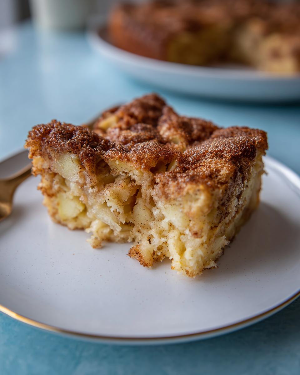 Nahaufnahme eines Stücks Apfelkuchen mit Zimt-Zucker-Topping, das auf einem weißen Teller liegt.