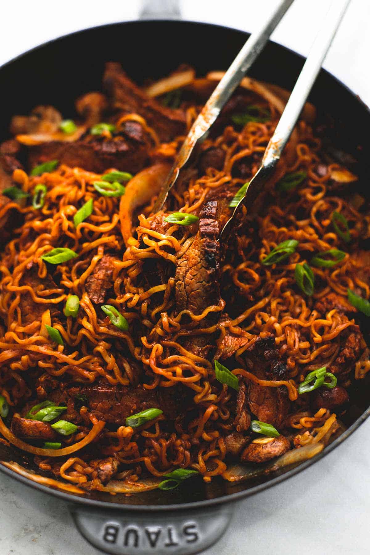 Korean beef noodles stir fry with tender beef slices, spicy sauce, and scallions cooked in a skillet