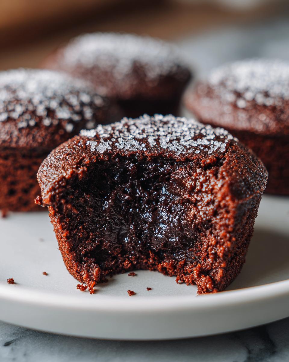 Ein angebissener Schokomuffin mit flüssigem Kern, bestreut mit Zuckerkruste, typisch für Schokomuffins mit Kakao & Zuckerkruste.