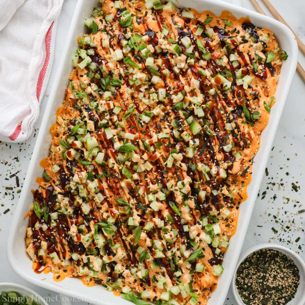 Würziges Lachs Sushi Bake in einer Auflaufform mit cremiger scharfer Sauce, Gurkenwürfeln, Frühlingszwiebeln und Sesam als einfaches Dinner-Rezept.